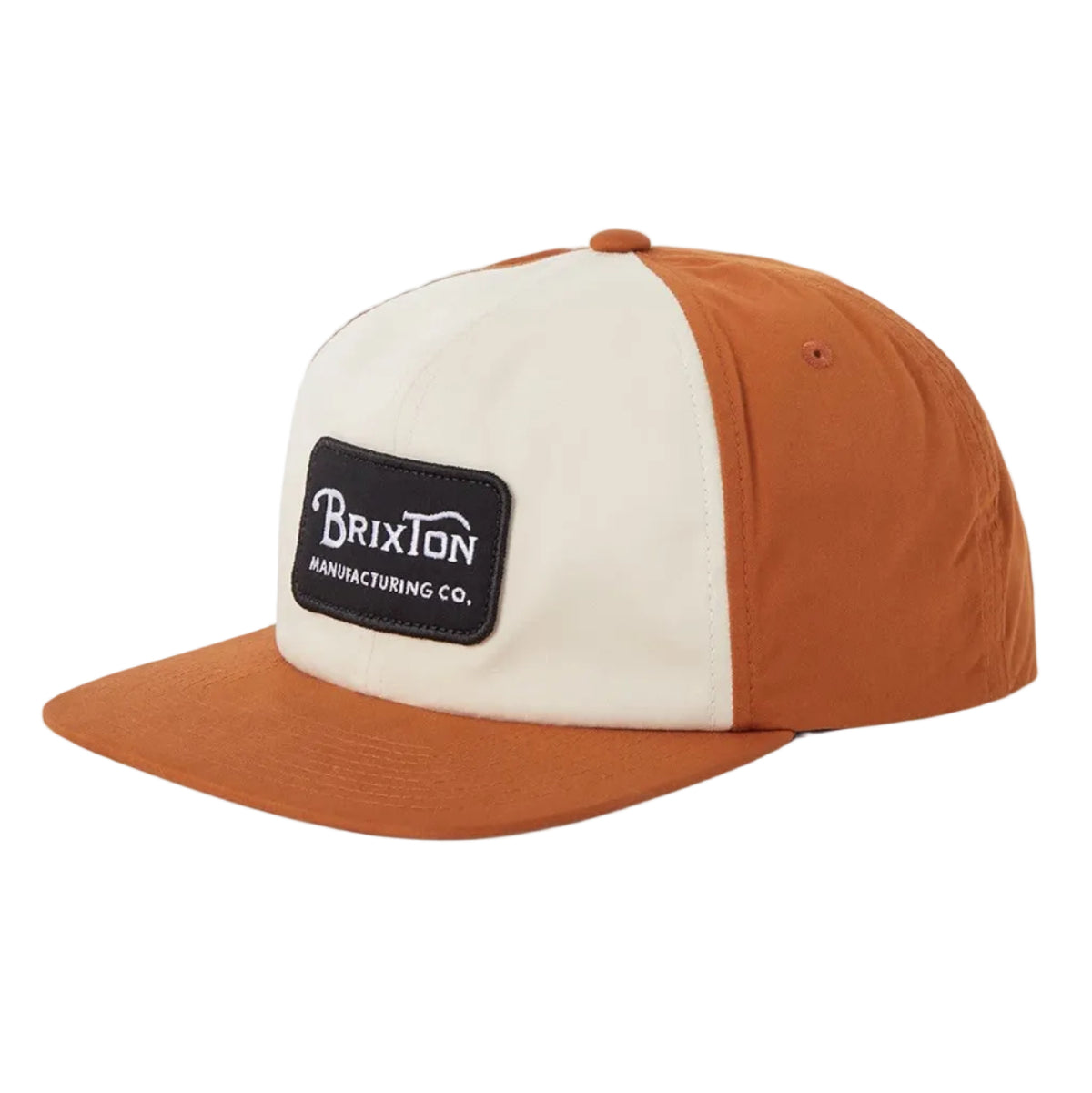 A Brixton snapback cap with a two-tone design featuring a cream front panel and a rust-orange crown and brim, with a black rectangular logo patch on the front.