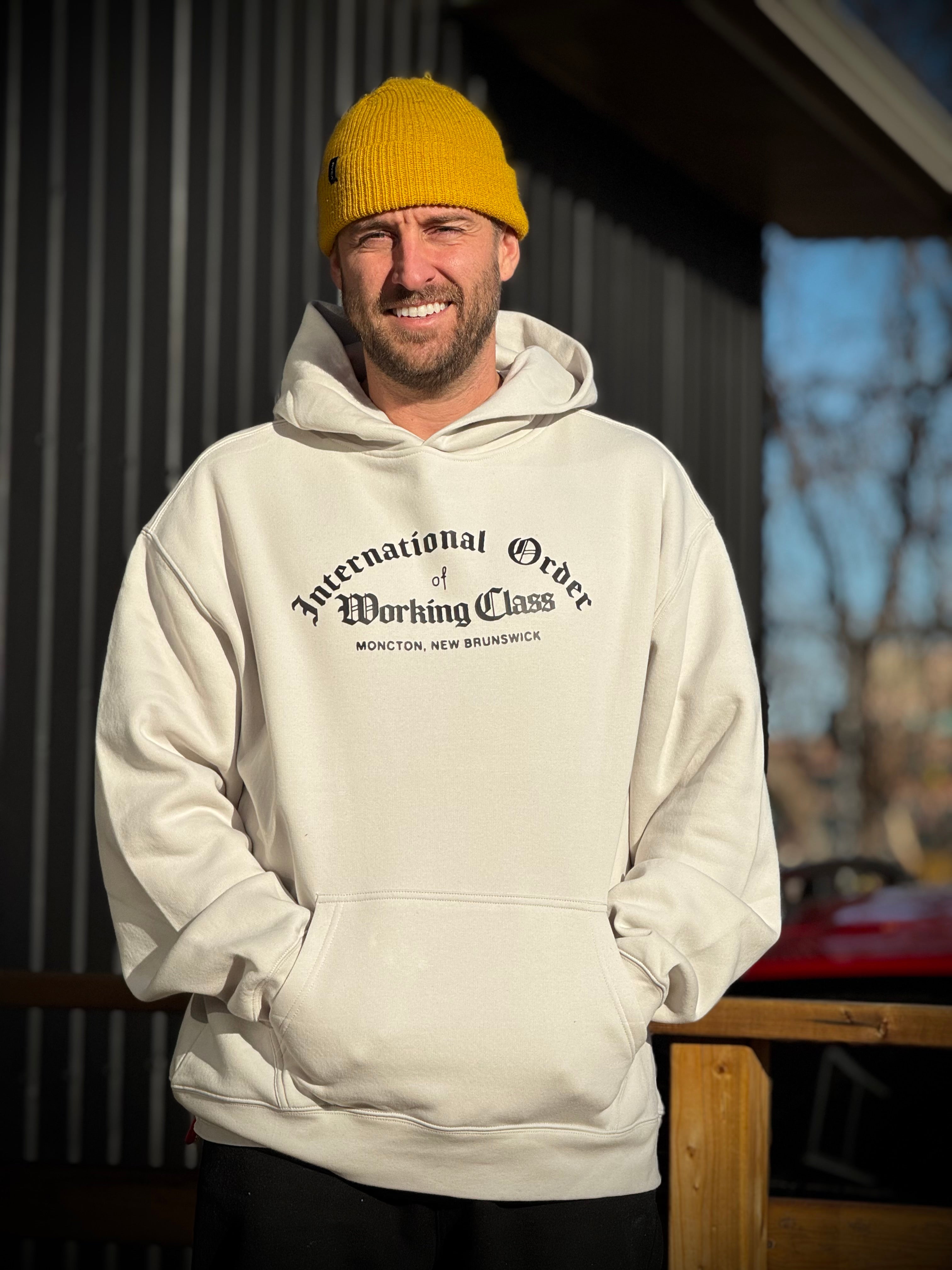 Person wearing a beige hoodie with text and a yellow beanie outdoors.