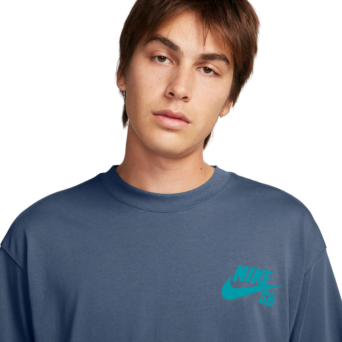 A close-up of a young man wearing a slate blue crewneck sweatshirt with a bright teal Nike SB logo on the left chest, set against a clean white background.