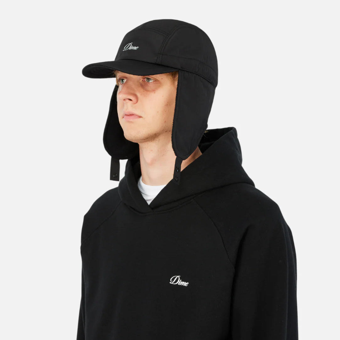 Person wearing a black hoodie and cap with a logo on a white background