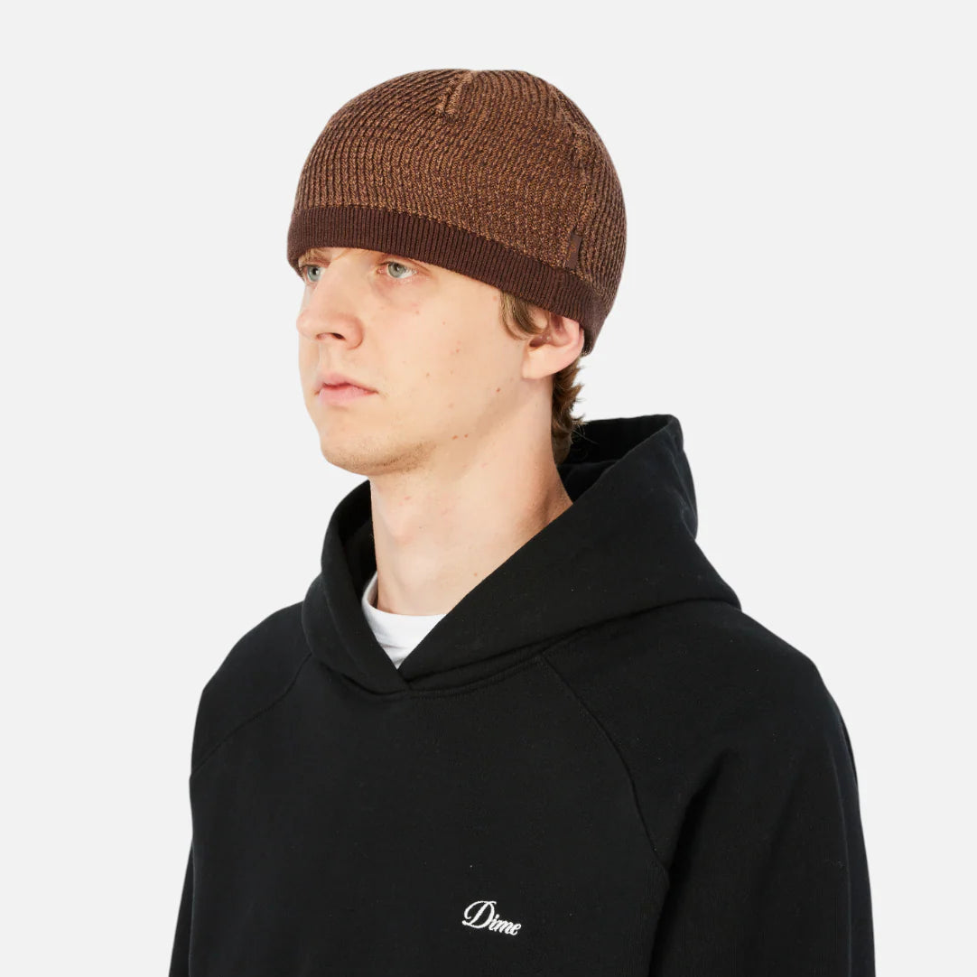 Person wearing a black hoodie with a logo and a brown beanie on a white background