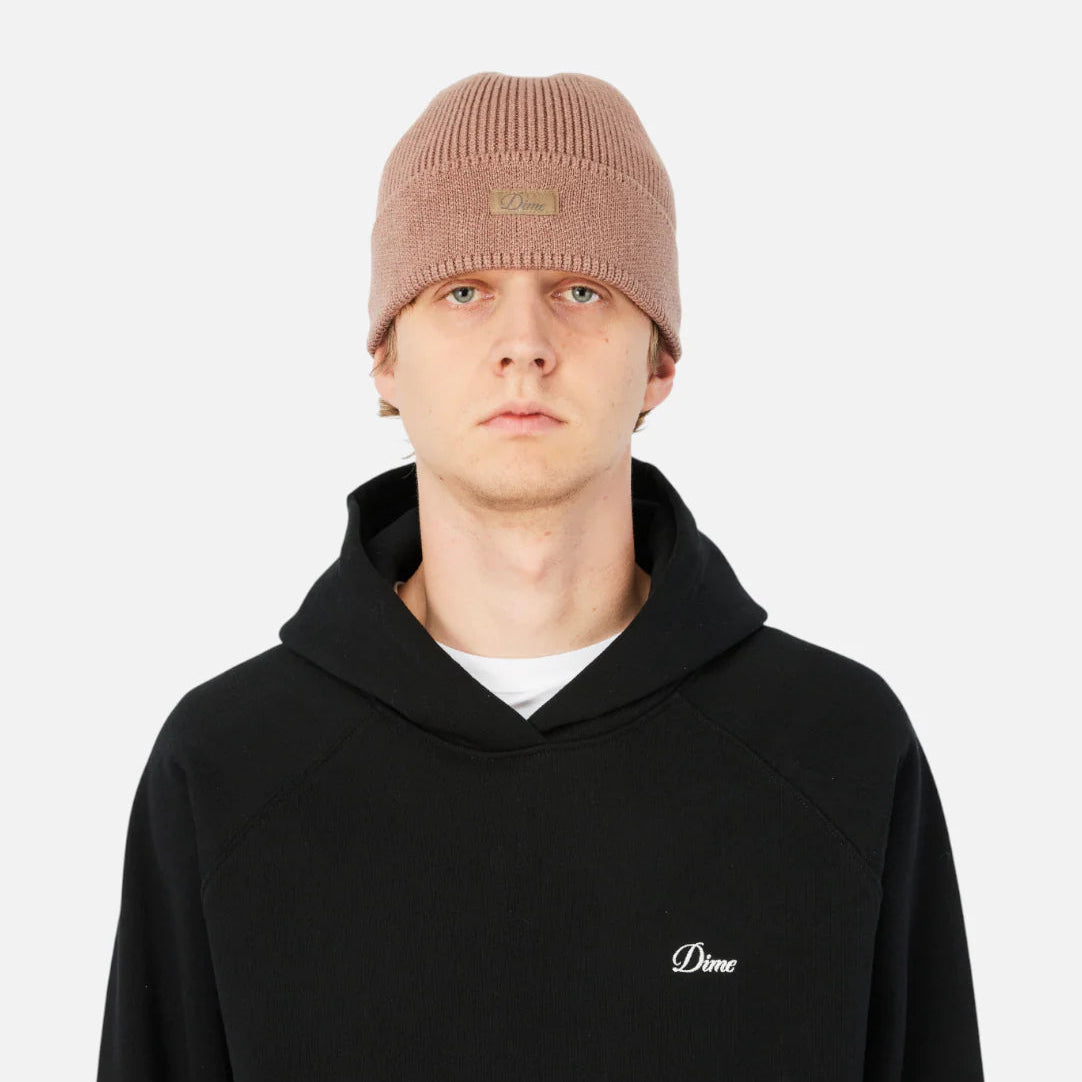 Person wearing a black hoodie with a small logo and a beige beanie on a white background