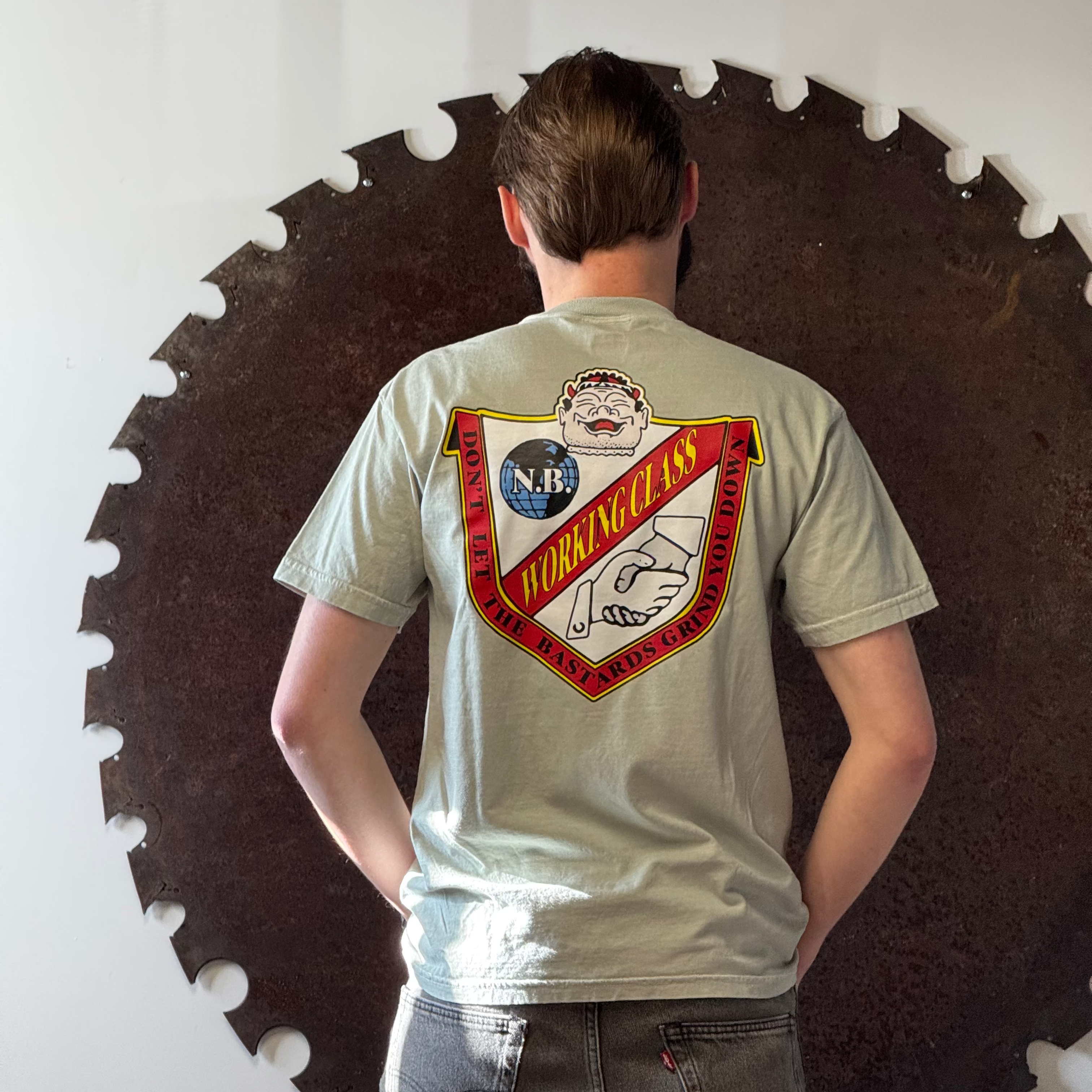Person wearing a t-shirt with a logo in front of a large circular saw blade.