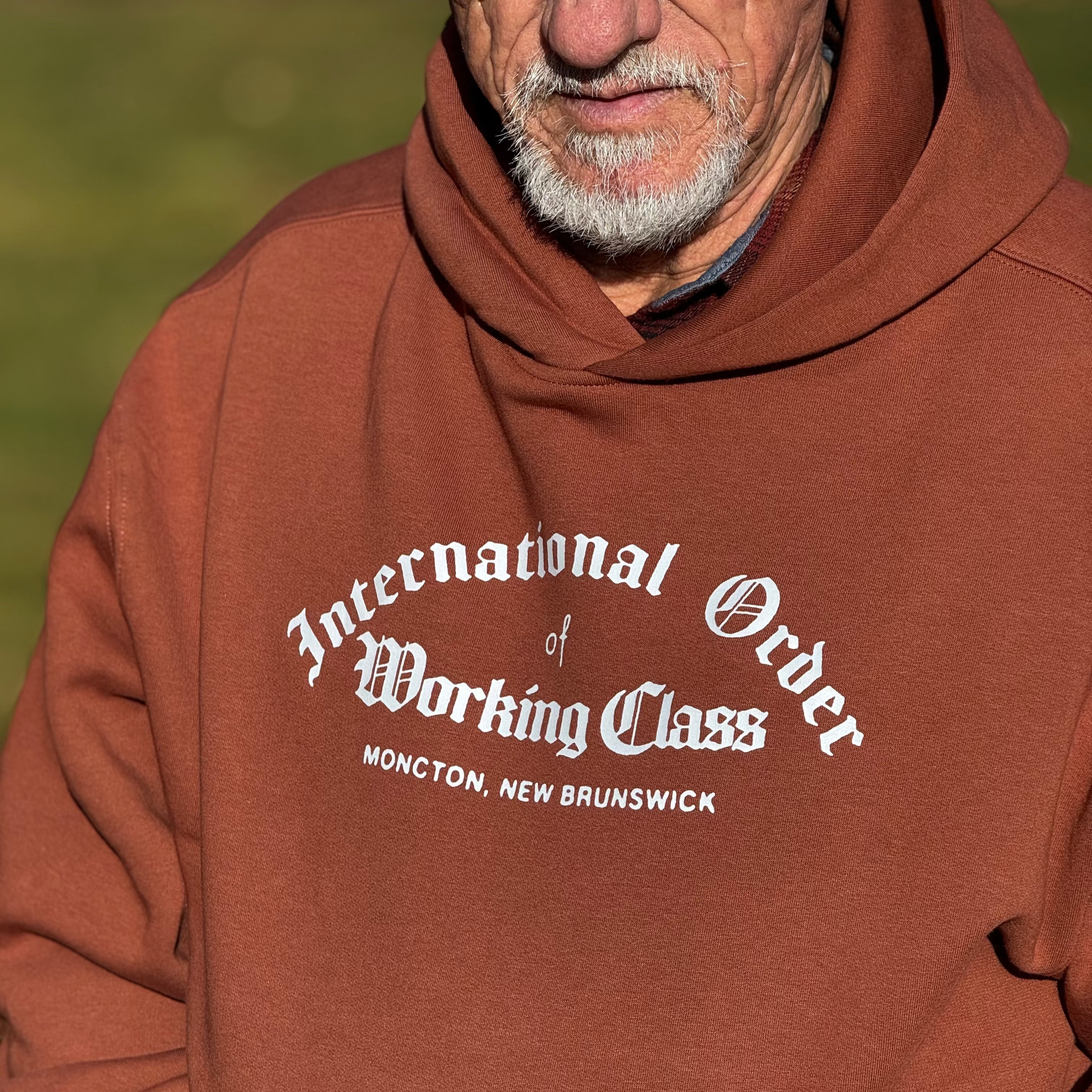 Man wearing a brown hoodie with text on it, standing outdoors.