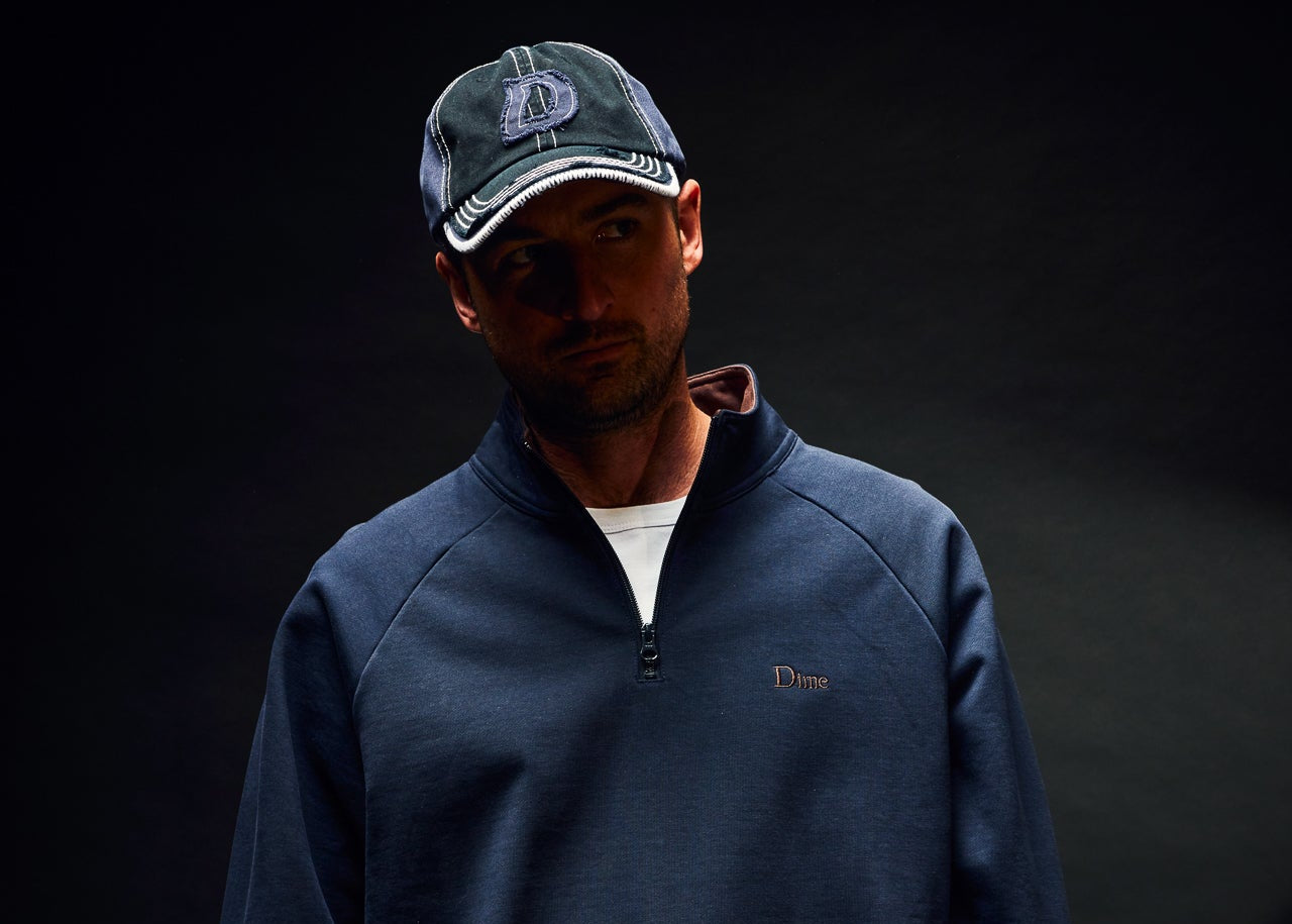 Man wearing a navy blue pullover with a logo on a black background