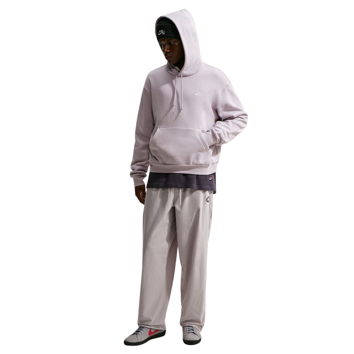 A model wearing a light lavender-gray hoodie and matching sweatpants, styled with a dark gray t-shirt underneath and gray sneakers, set against a plain white background.