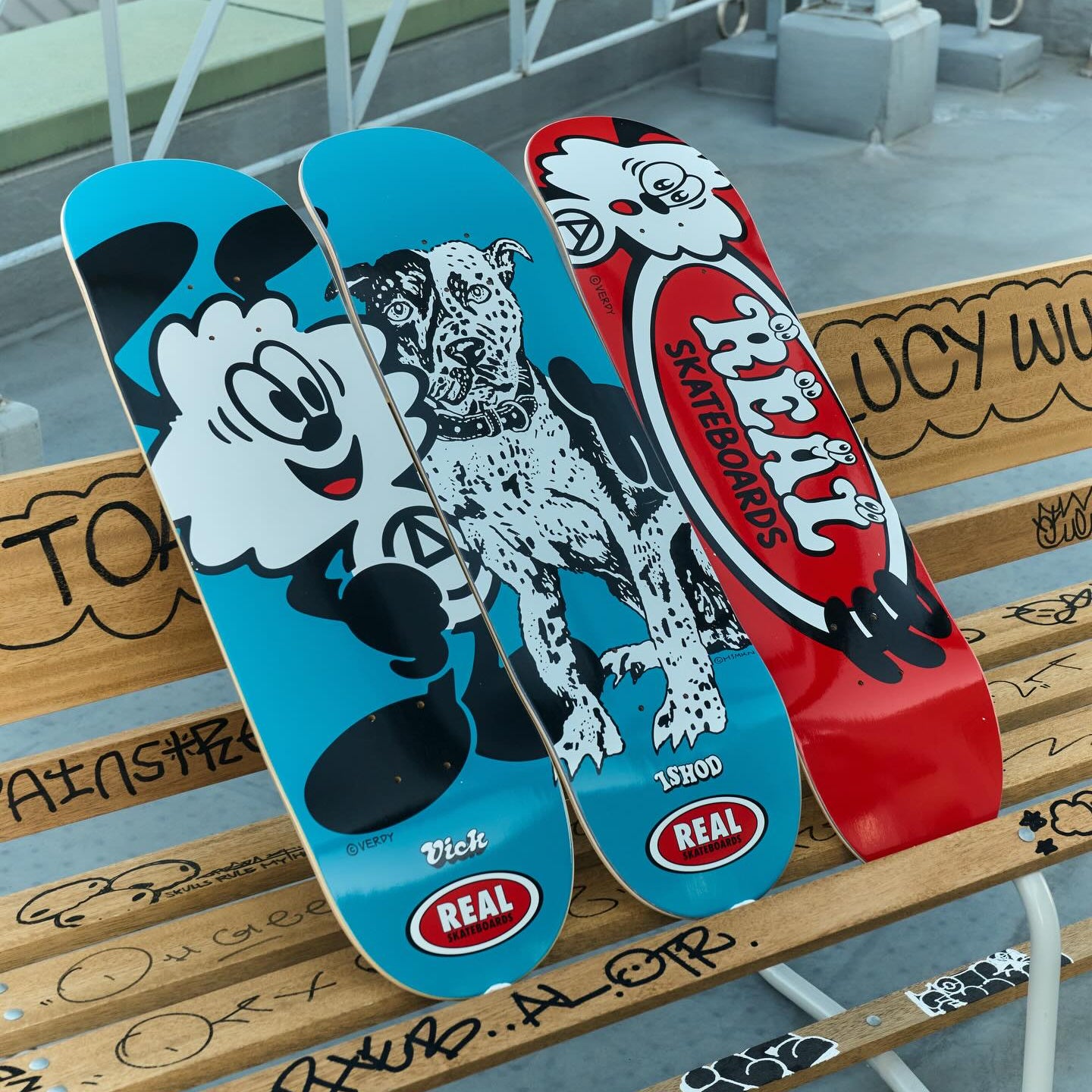 Three skateboard decks with cartoon characters and 'Real' branding on a bench.