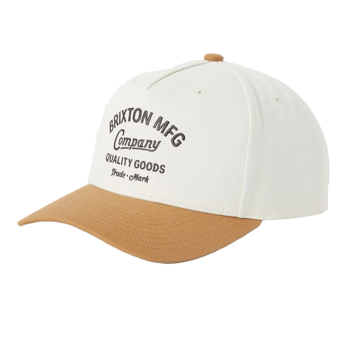 A baseball cap with an off-white crown and a tan curved brim, featuring black embroidered text on the front that reads 'BRIXTON MFG Company QUALITY GOODS'.