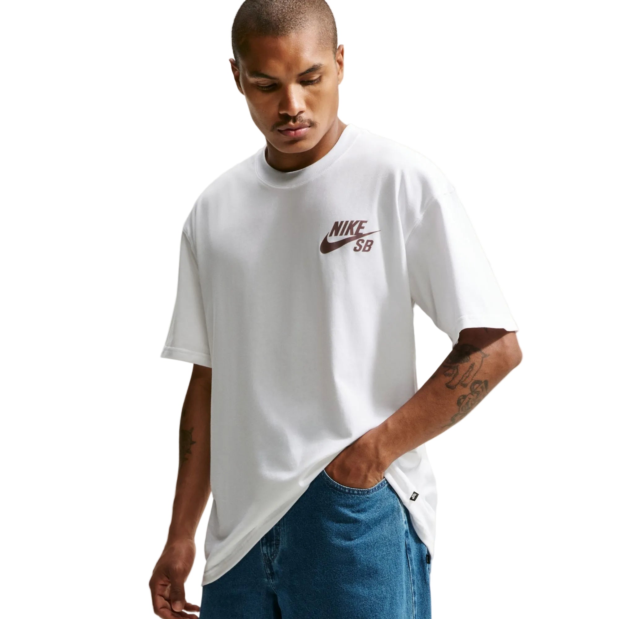 A man wearing a white Nike SB t-shirt with a brown swoosh logo on the chest, paired with blue jeans, against a light gray background.