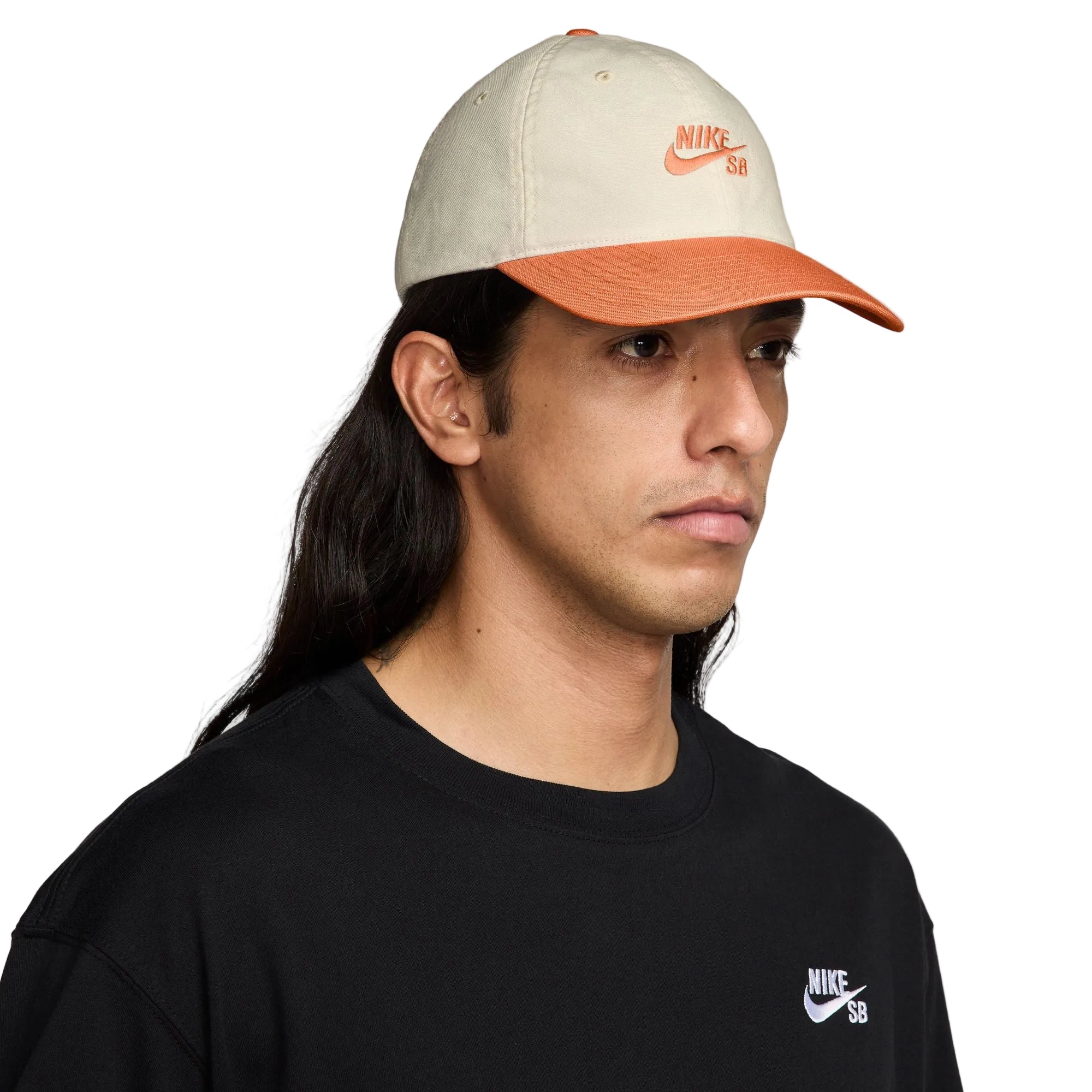 Person wearing a beige and orange Nike cap with a black shirt featuring Nike SB logo on a white background