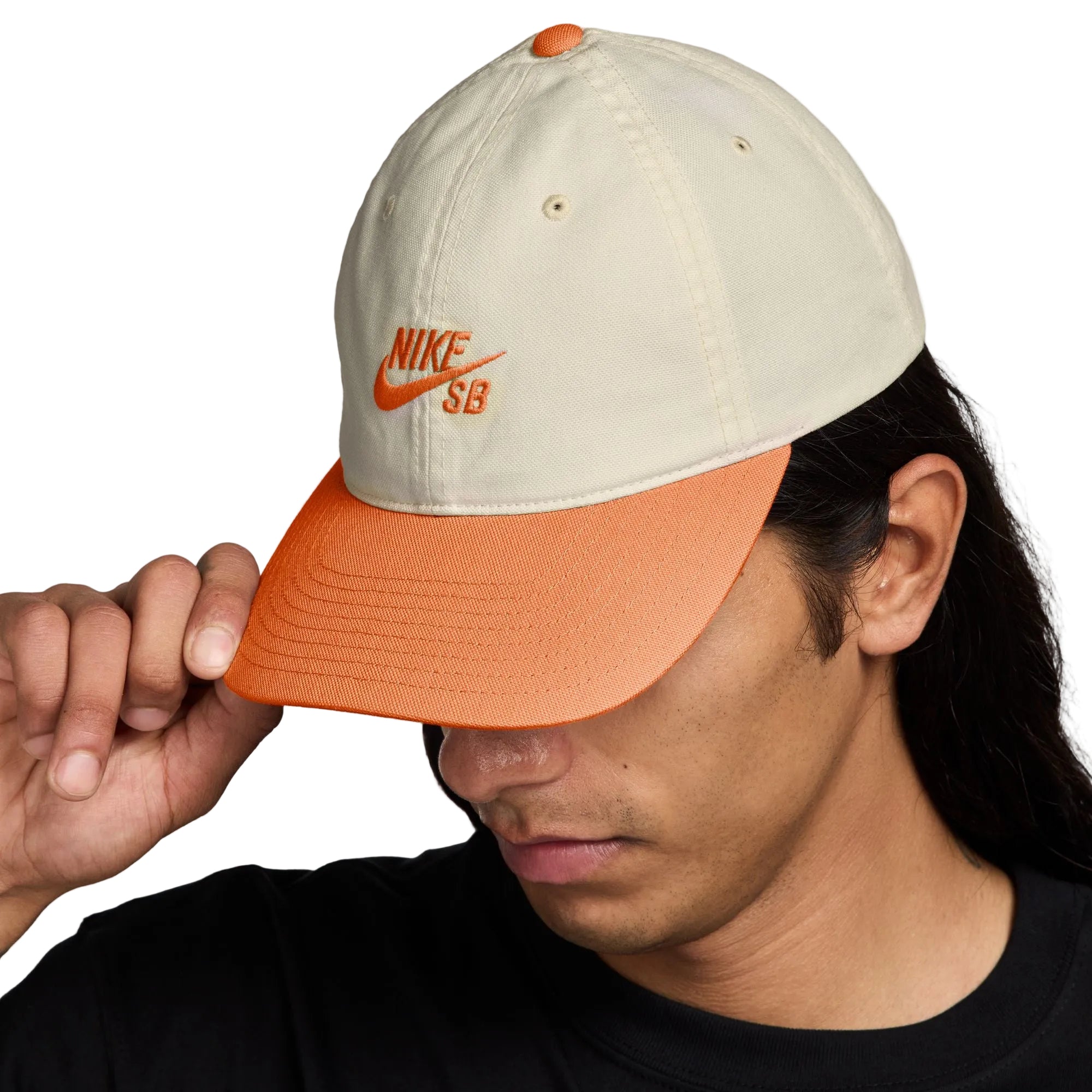 Person wearing a beige and orange Nike SB cap on a white background