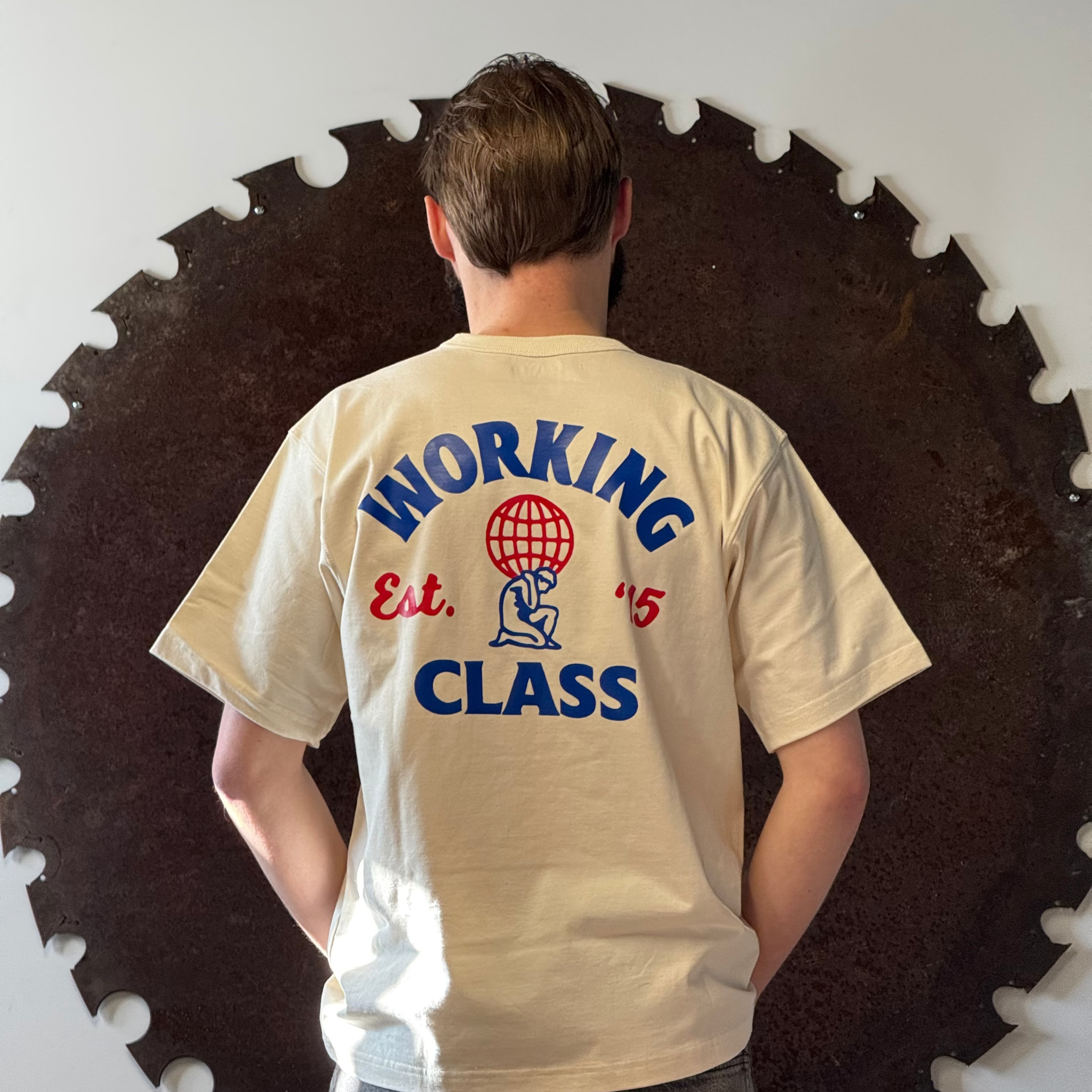 Person wearing a t-shirt with 'Working Class' text and graphics, standing in front of a circular saw blade.