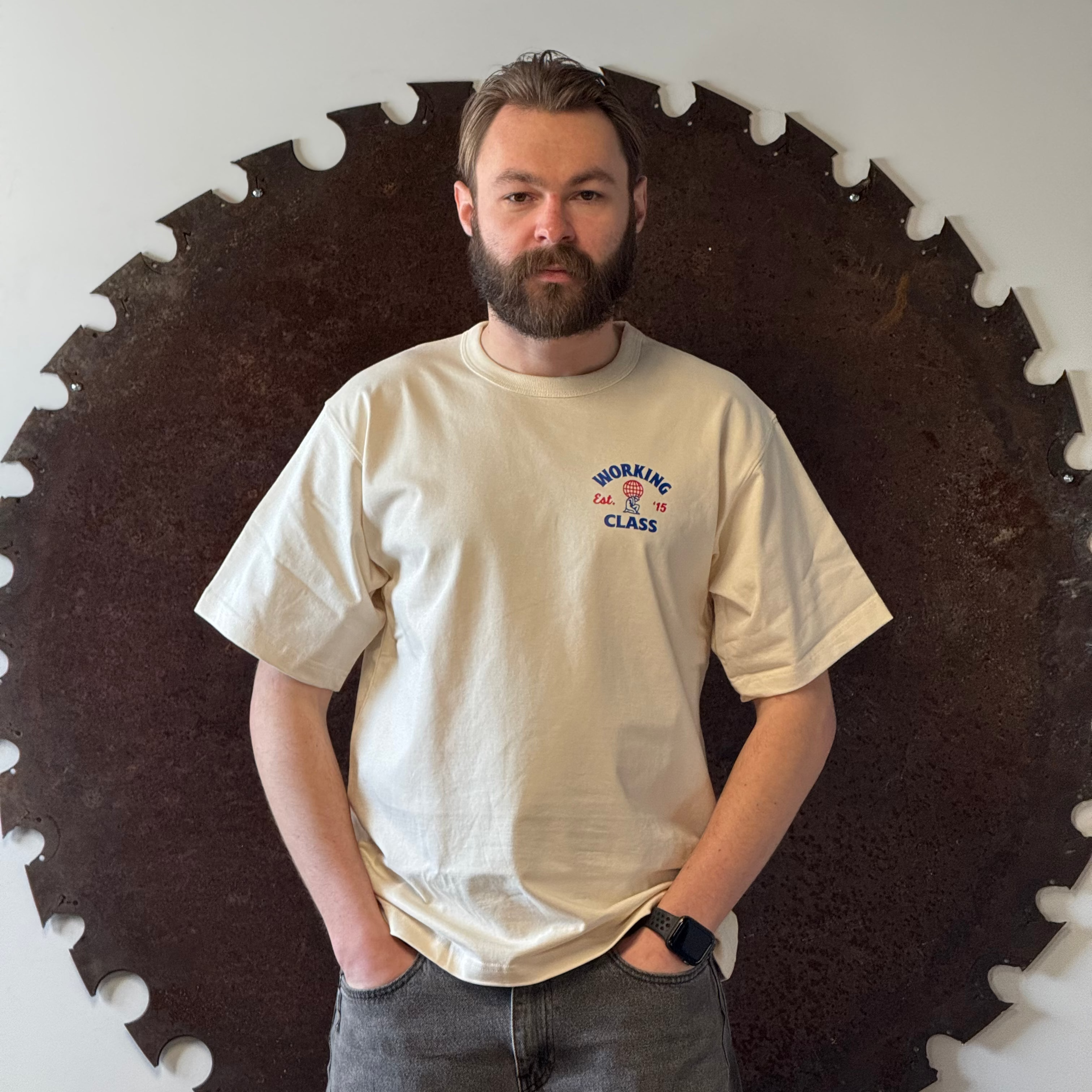 Man standing in front of a large circular saw blade on a white wall.