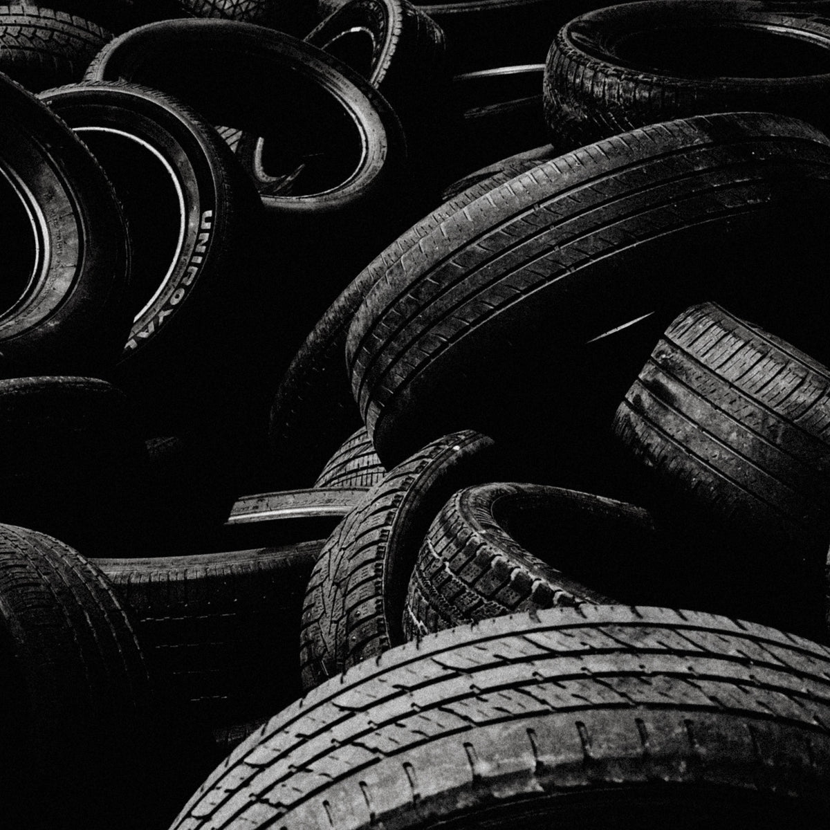 A black and white close-up of a pile of stacked and overlapping tires, showing detailed tread patterns and dark rubber surfaces.