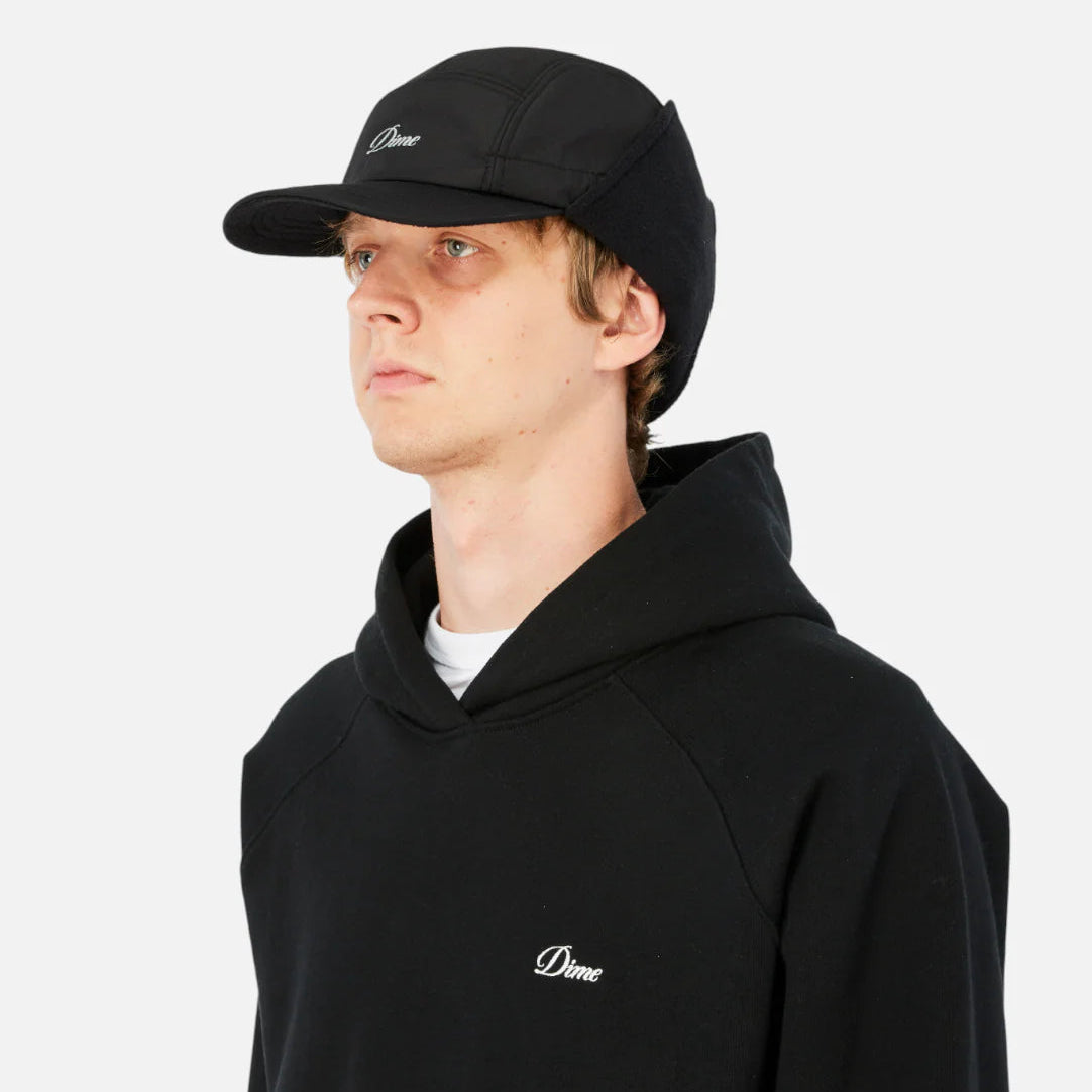 Person wearing a black hoodie and cap with a logo on a white background