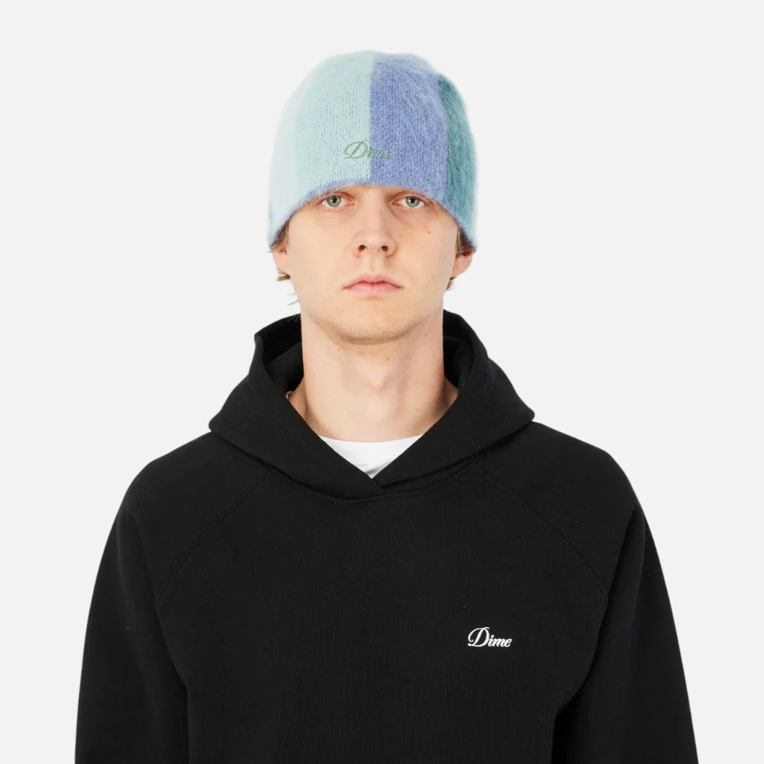 Person wearing a black hoodie with a logo and a multicolored beanie on a white background