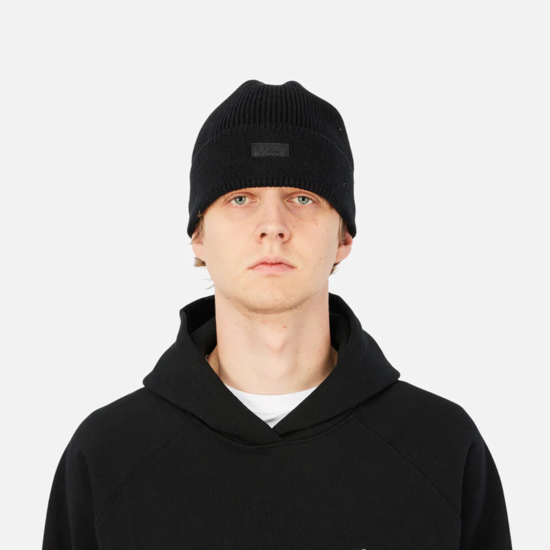 Person wearing a black hoodie with a small logo on a white background
