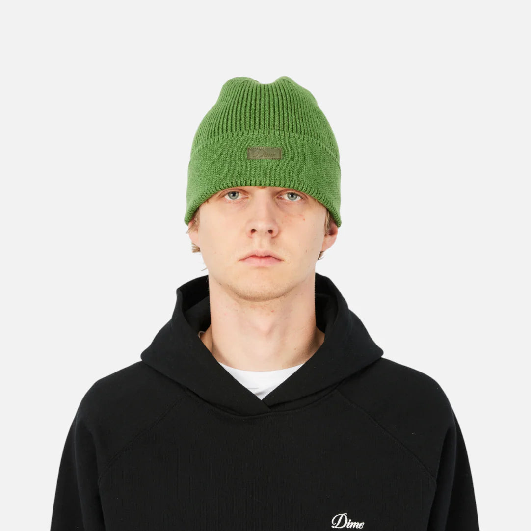 Person wearing a black hoodie with a logo and a green beanie on a white background