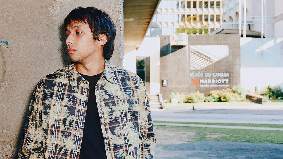 Man wearing a patterned shirt leaning against a wall with a building in the background