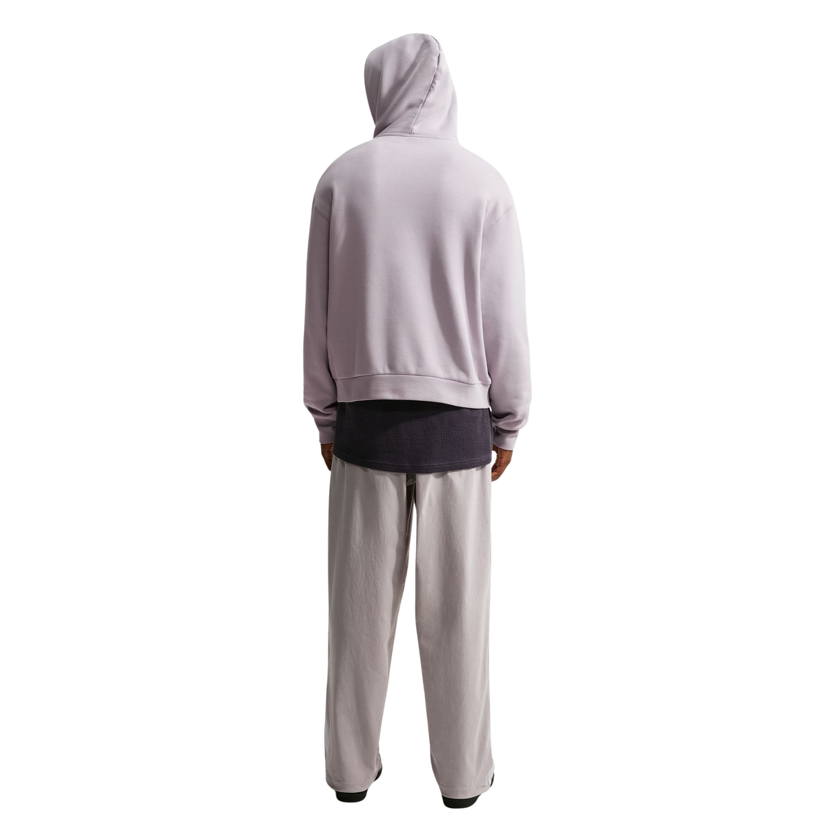 A person shown from the back wearing a light lavender hooded sweatshirt over a dark charcoal T-shirt and light gray sweatpants, isolated on a white background.