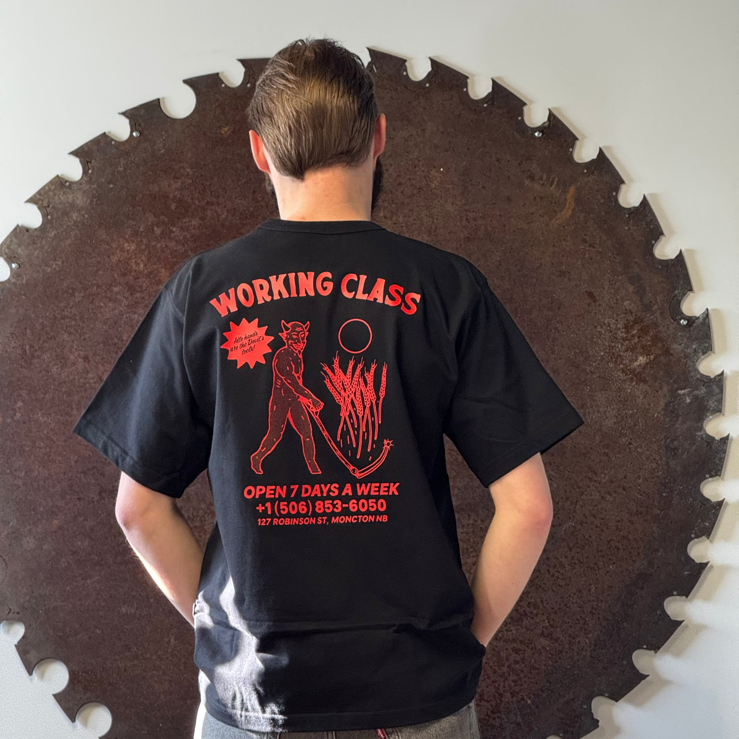 Person wearing a black t-shirt with red graphics and text, standing in front of a large circular saw blade.