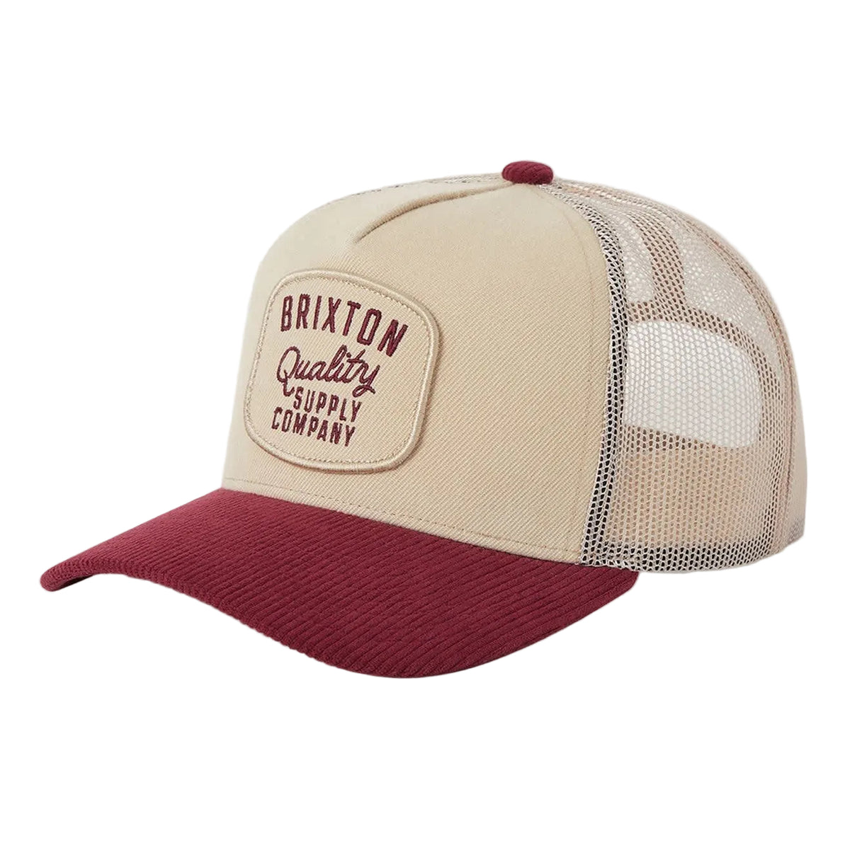 A Brixton Quality Supply Company trucker hat with a beige front panel and mesh back, featuring a dark red curved brim and matching red button on top.