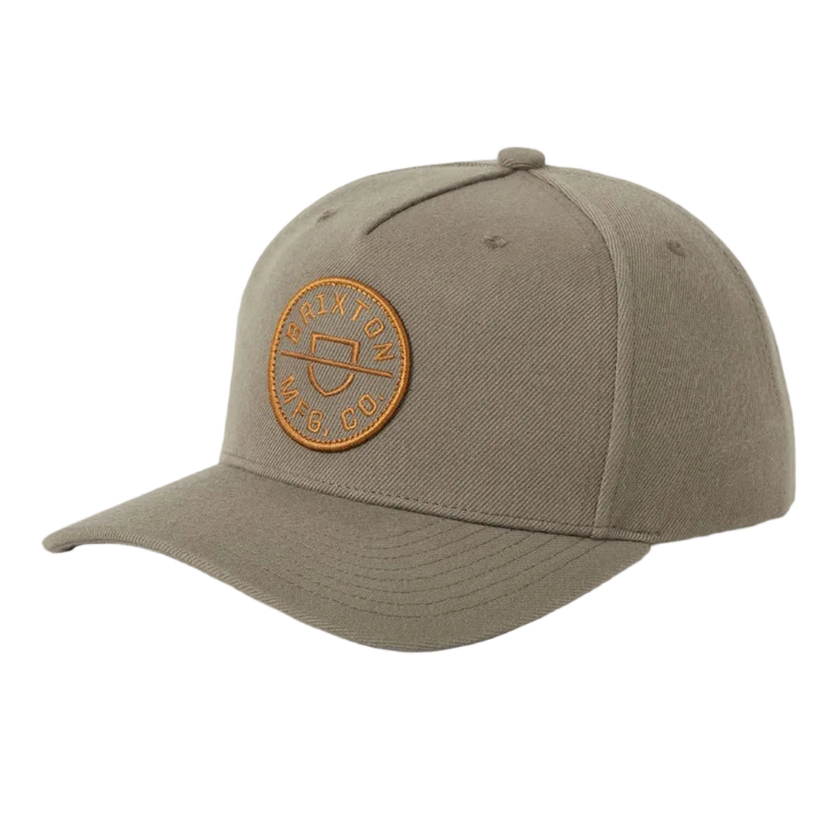 A structured baseball cap in a muted taupe-gray color, featuring a circular tan leather patch on the front with the brand name 'Brixton MFG, Co' embroidered around a central shield logo.
