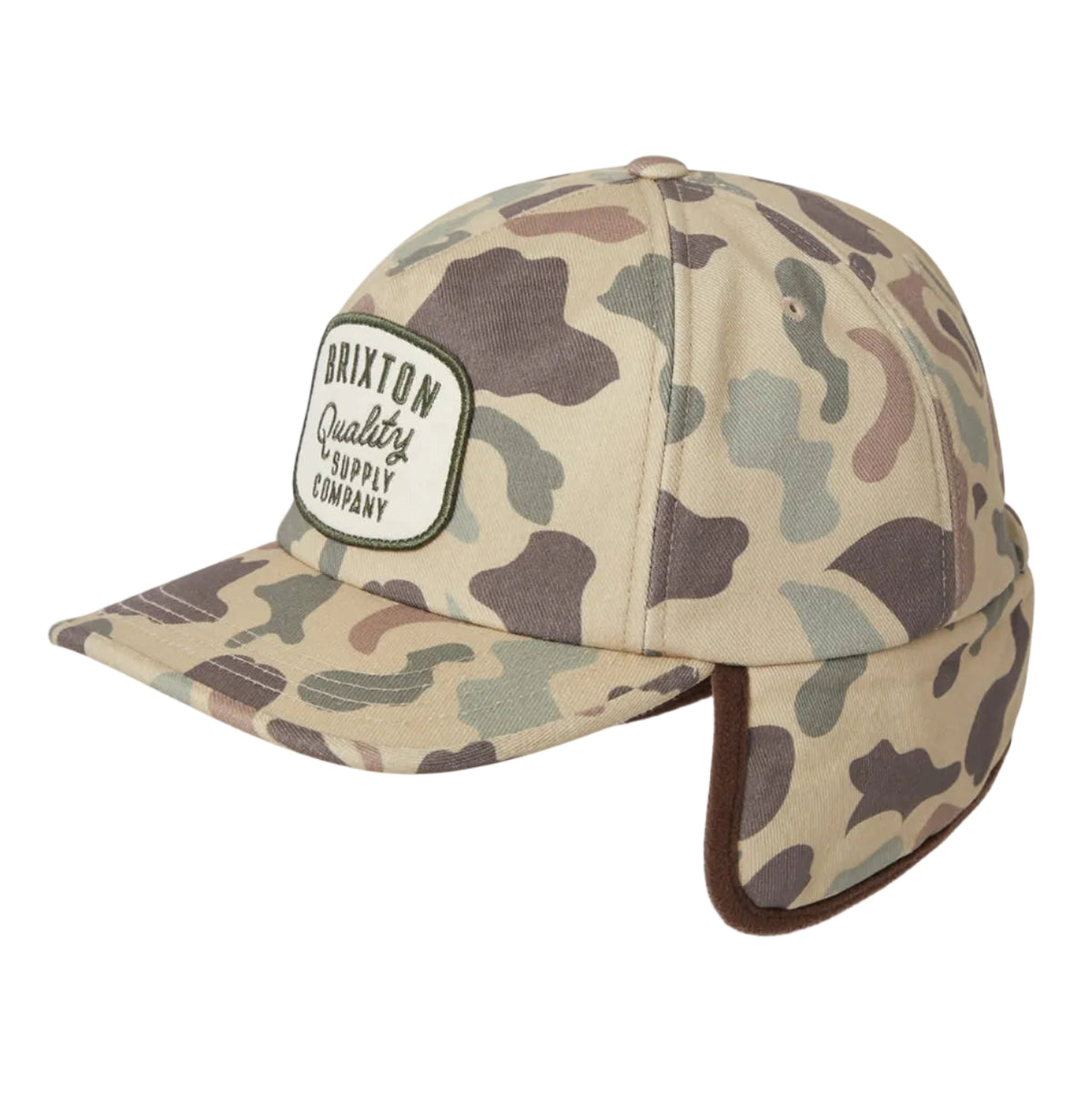 A camouflage-patterned snapback cap with ear flaps, featuring a white embroidered patch on the front that reads 'BRIXTON Quality Supply Company'.